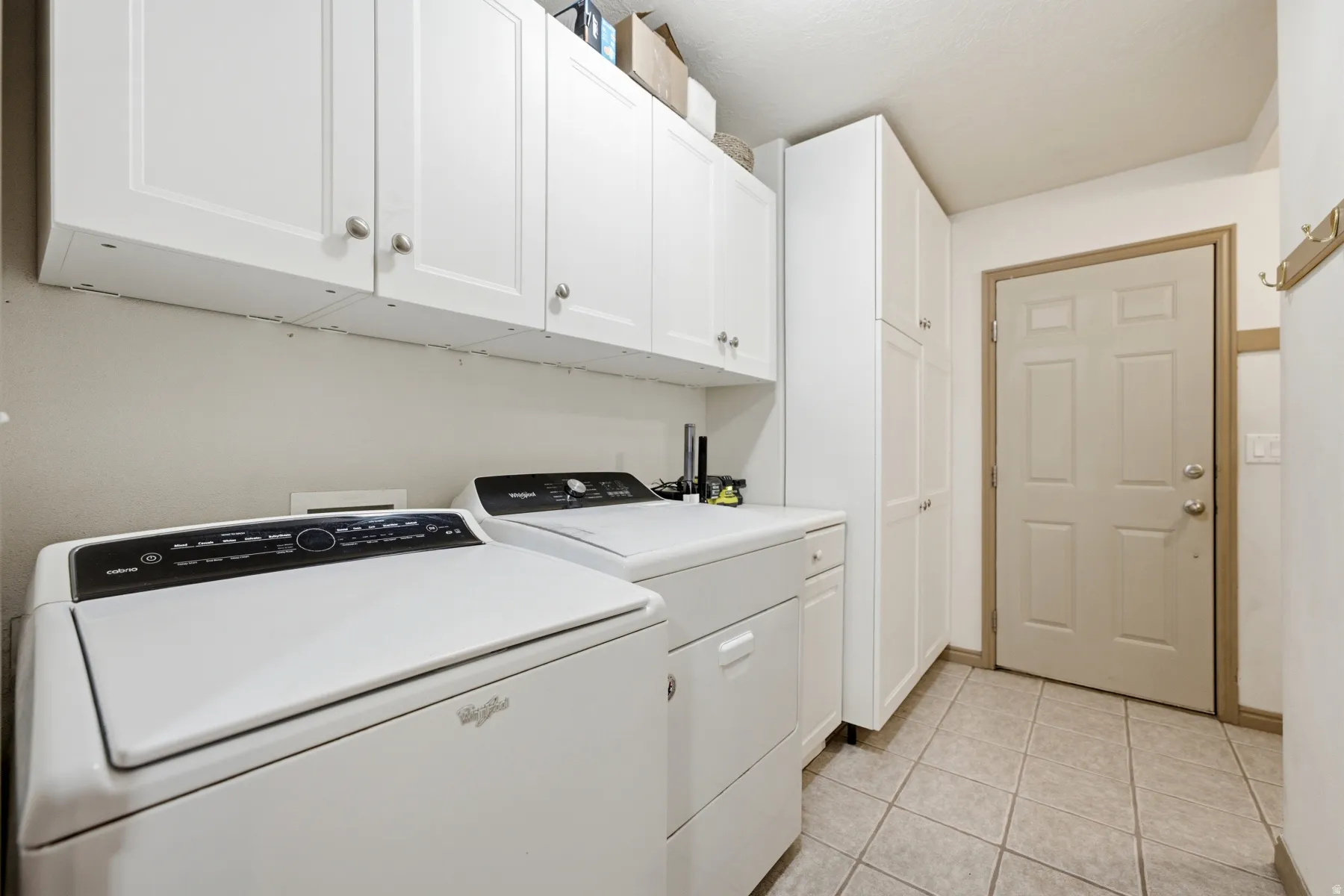 Laundry area featuring white cabinetry with silver-tone hardware, tall storage cabinets, and tiled flooring