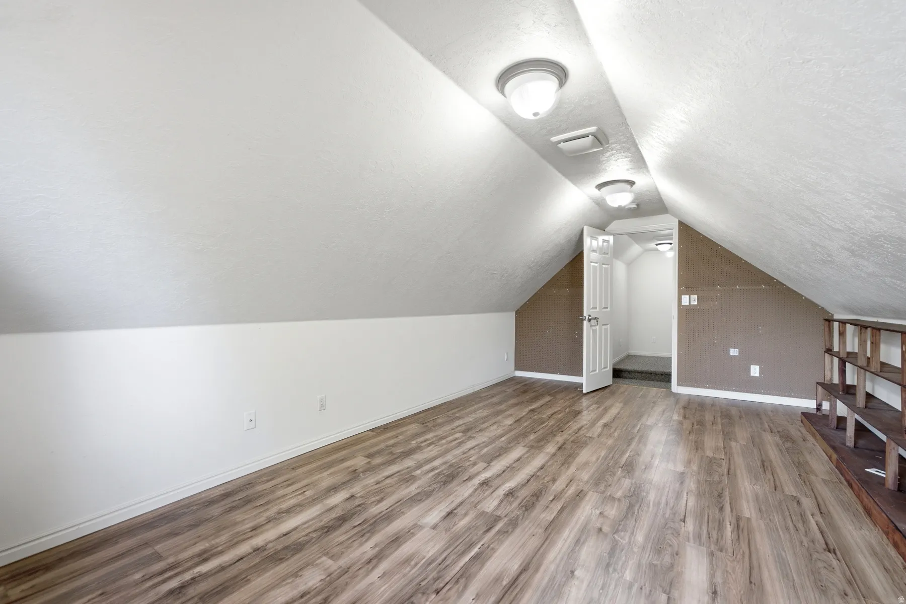 Attic space featuring wood-finish flooring, sloped white ceilings, and recessed lighting fixtures