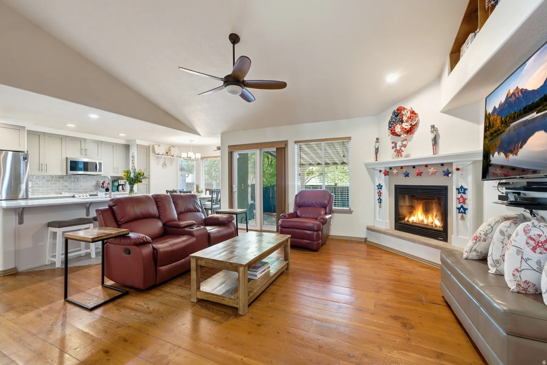 Open concept living space featuring wood-finish flooring, a vaulted ceiling with a ceiling fan, and a gas fireplace with a white mantel