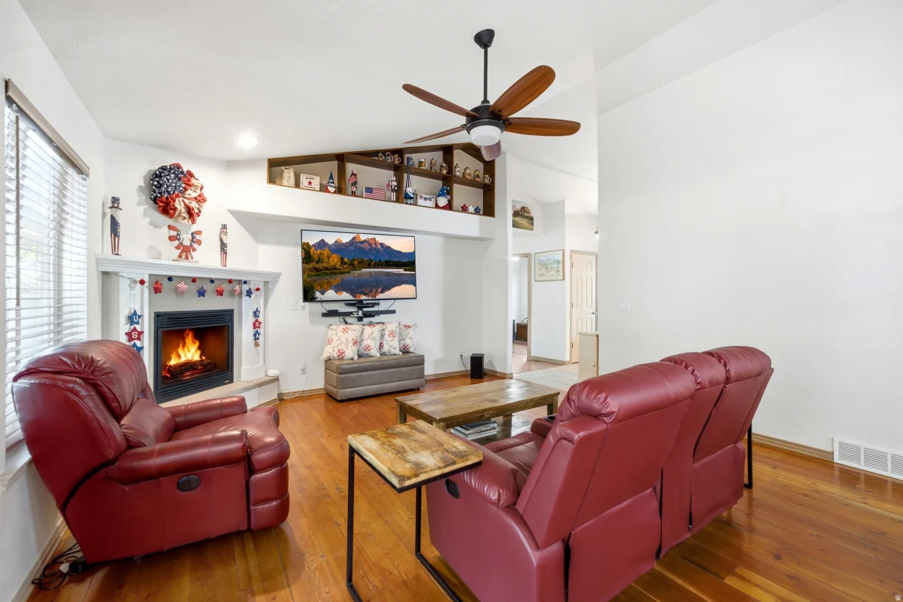 Living area featuring wood-finish flooring, a white-mantled fireplace, and an integrated ceiling fan