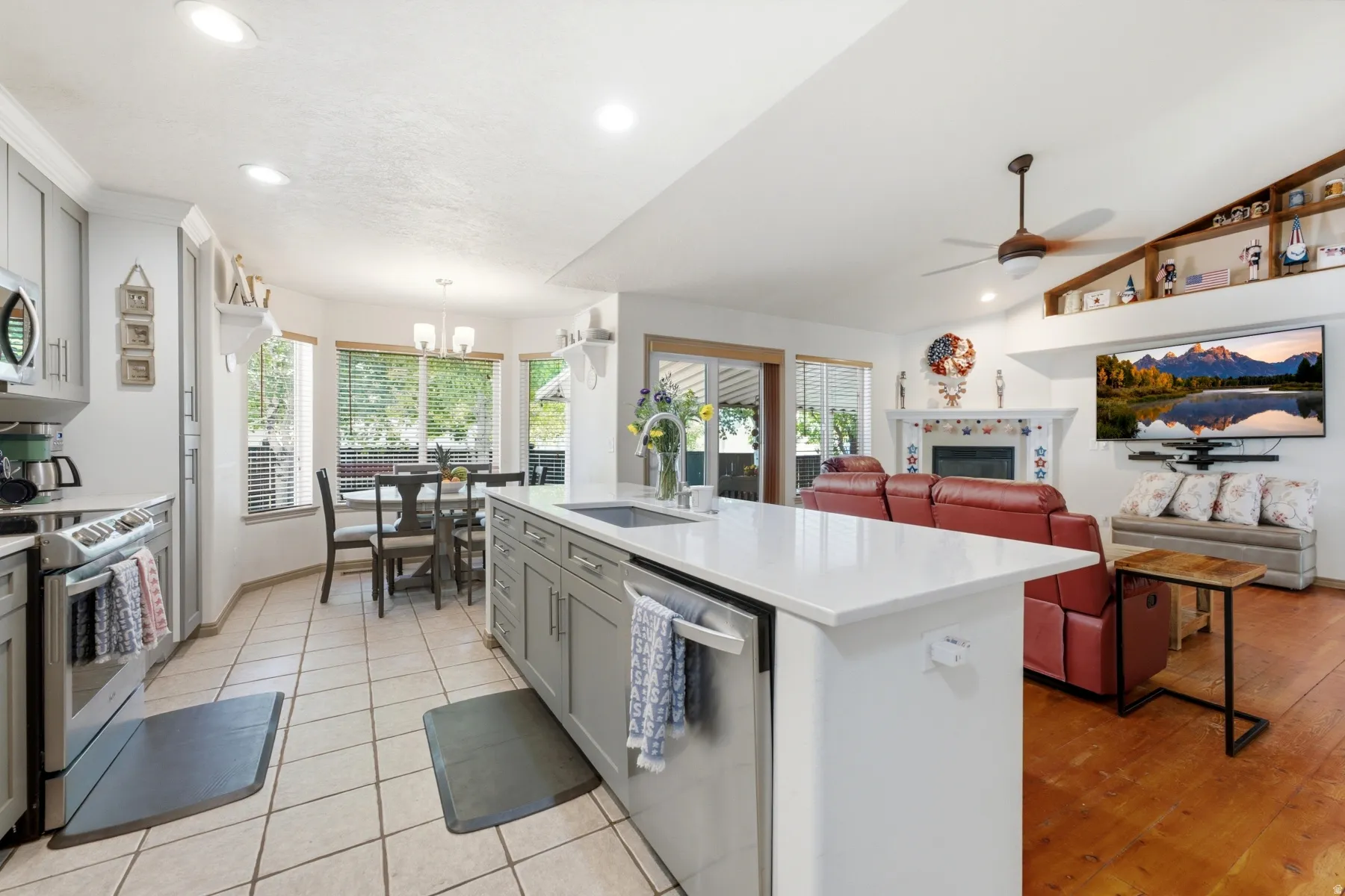 Spacious open-concept living area featuring a kitchen island with sink, white countertops, recessed lighting, a built-in fireplace, and a vaulted ceiling with a fan