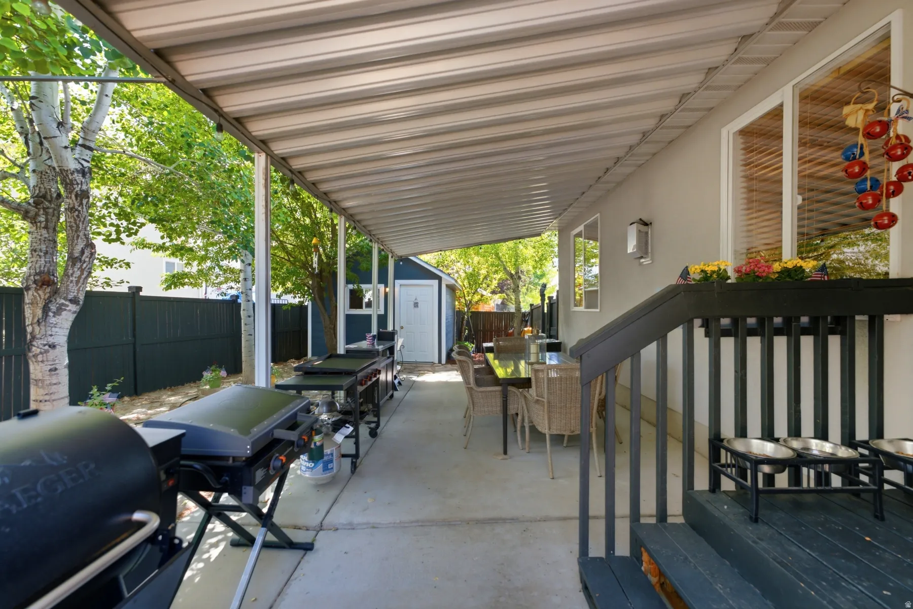 Expansive covered patio featuring a concrete surface, a built-in storage shed, a privacy fence, and mature trees