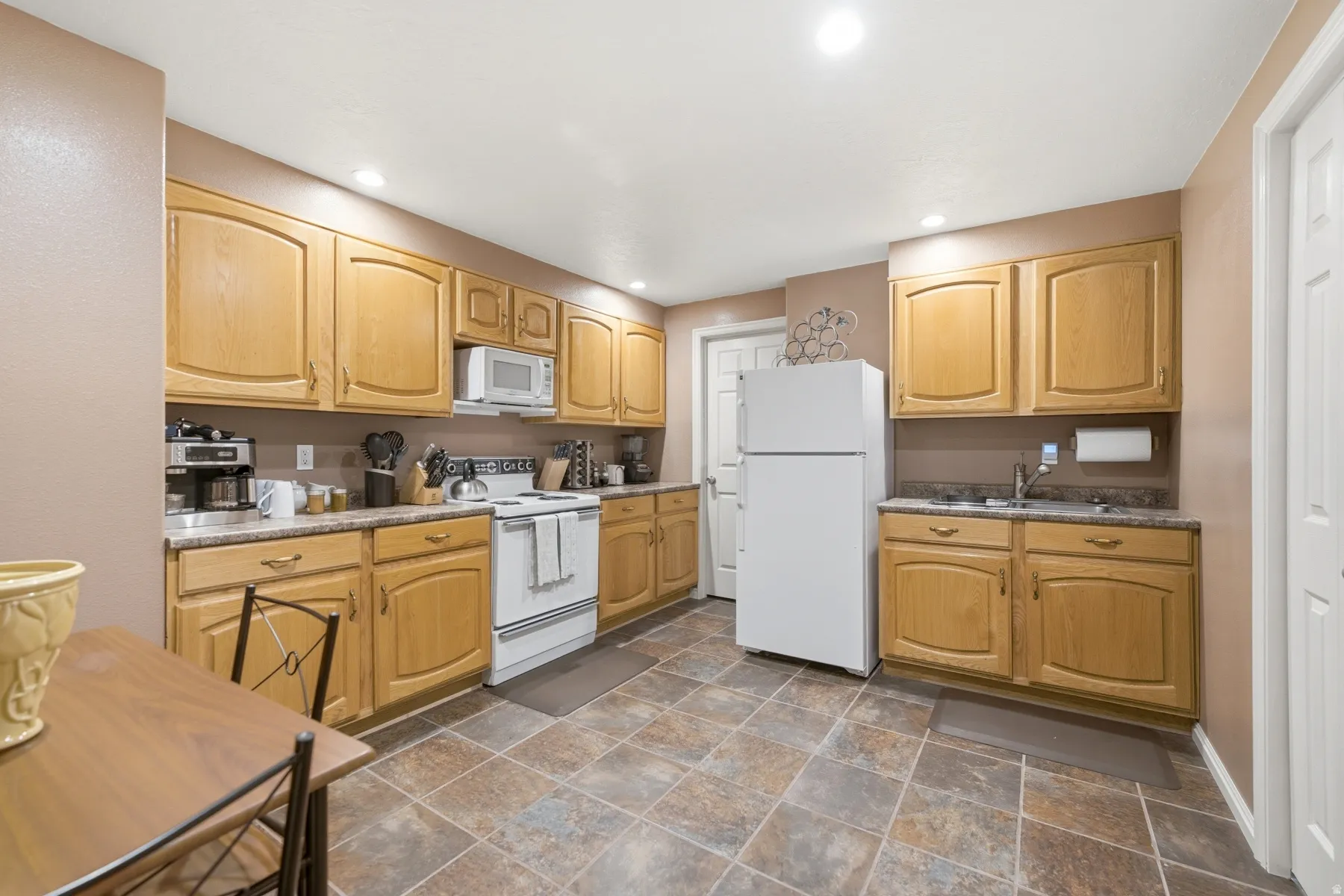 Spacious kitchen featuring light wood cabinetry, stone-finish countertops, and a white freestanding refrigerator