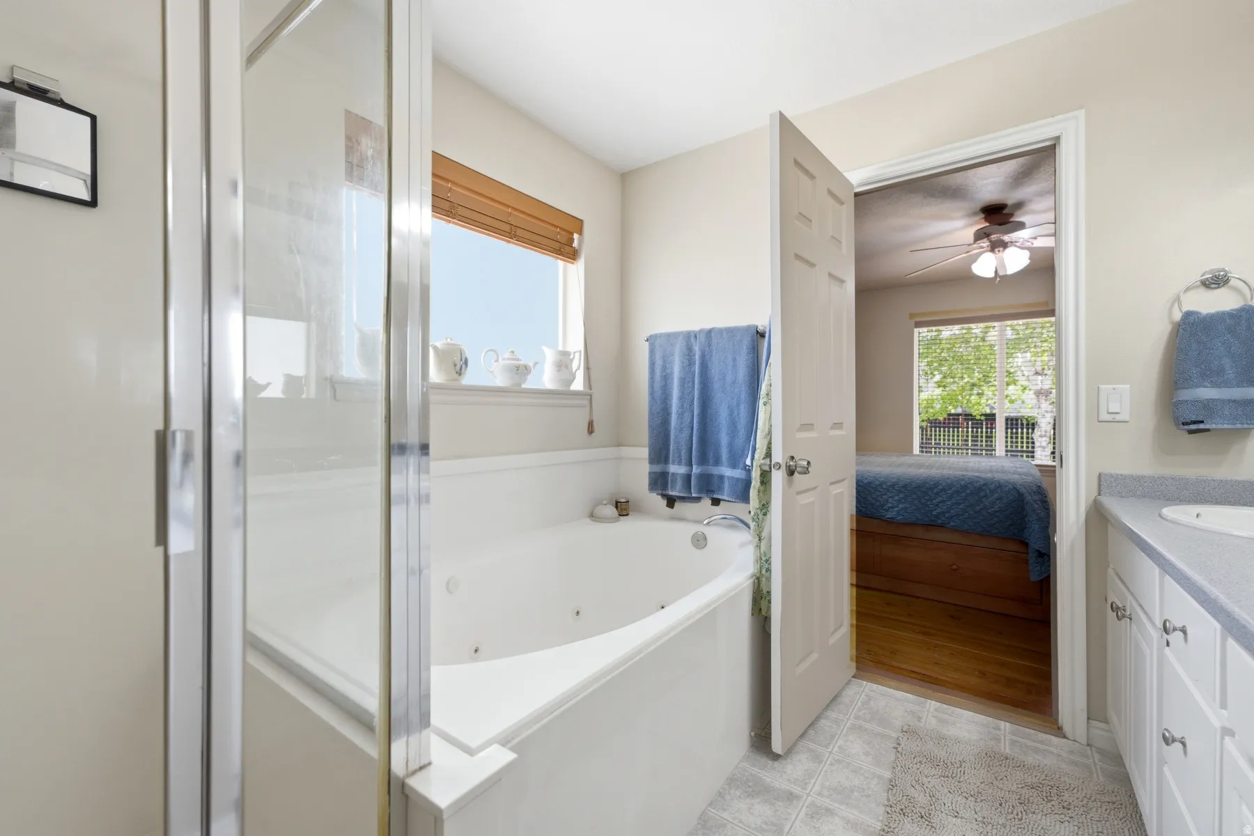 Primary suite bathroom with a glass-enclosed shower, built-in soaking tub, a window with a wood-slat blind, and a vanity with a countertop and under-sink cabinetry