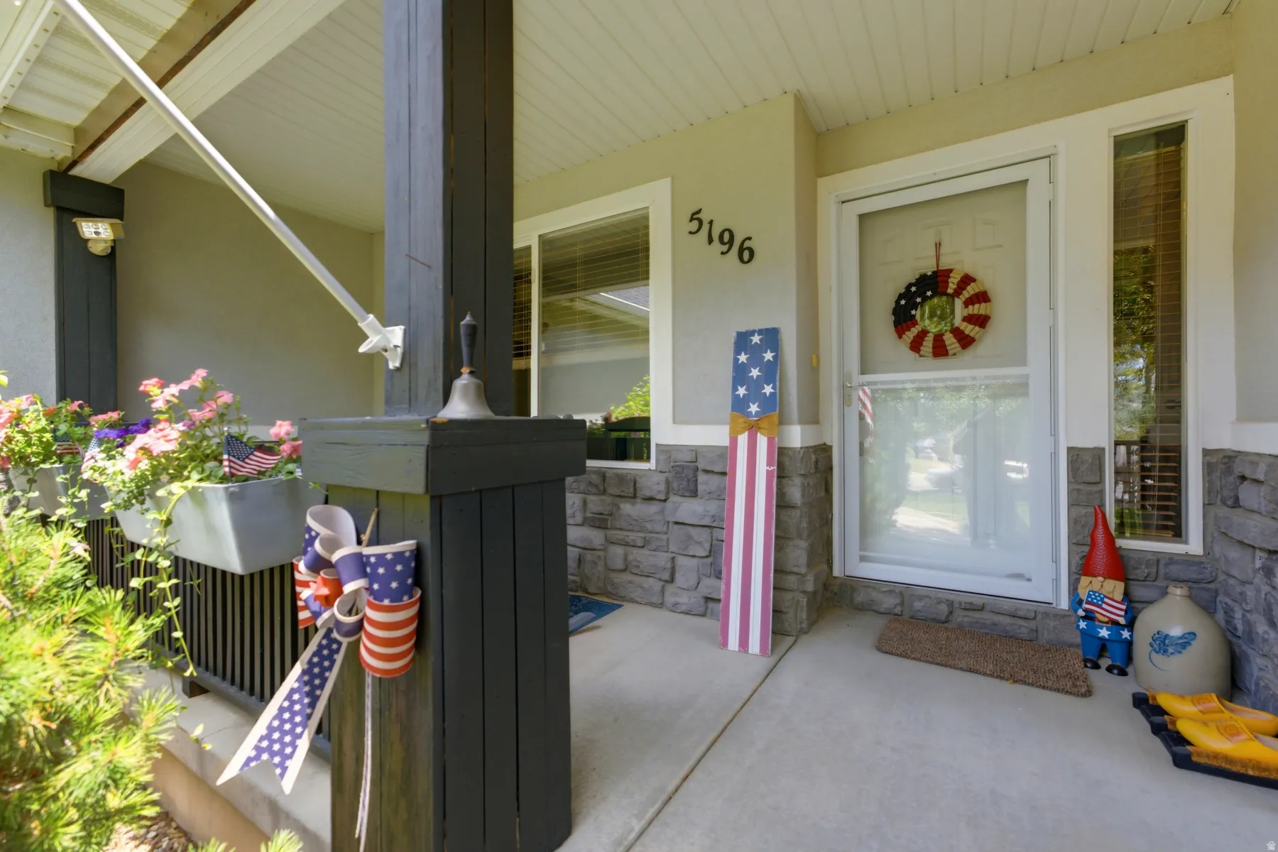 Covered front porch featuring a concrete pad, dark-toned support pillars, and stone veneer accents