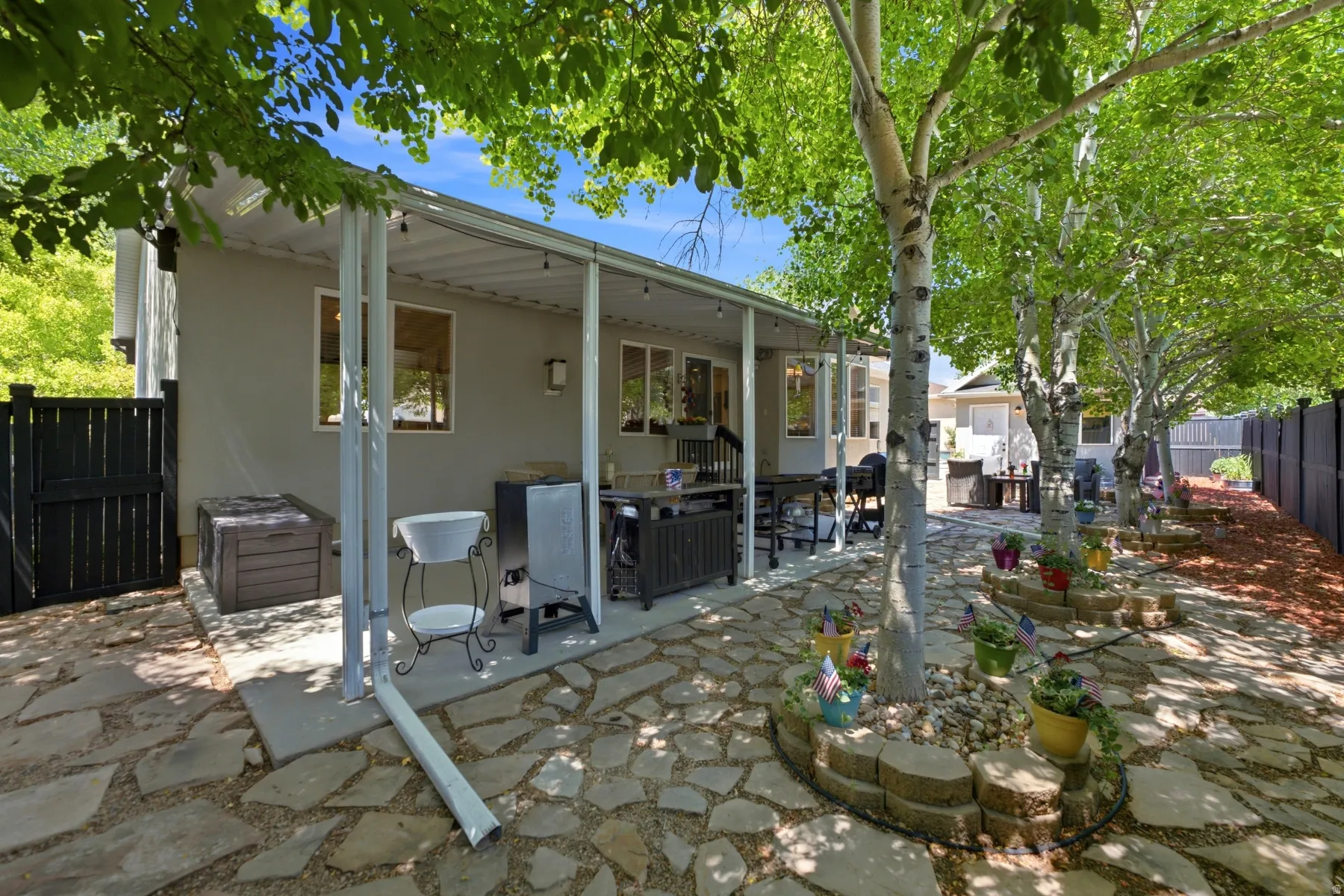Expansive flagstone patio with a covered outdoor living area, bordered by mature trees and a dark-toned privacy fence