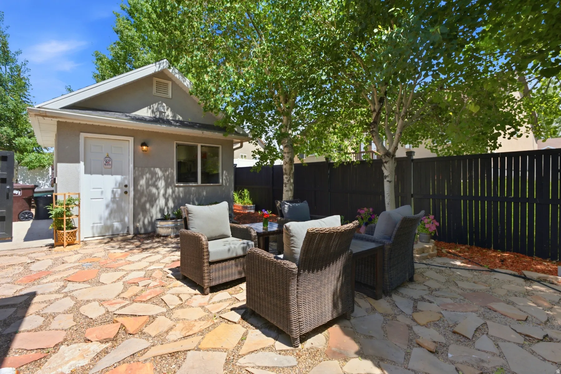 Flagstone patio featuring mature trees, a privacy fence, an exterior building with a single window, and a wall-mounted exterior light fixture