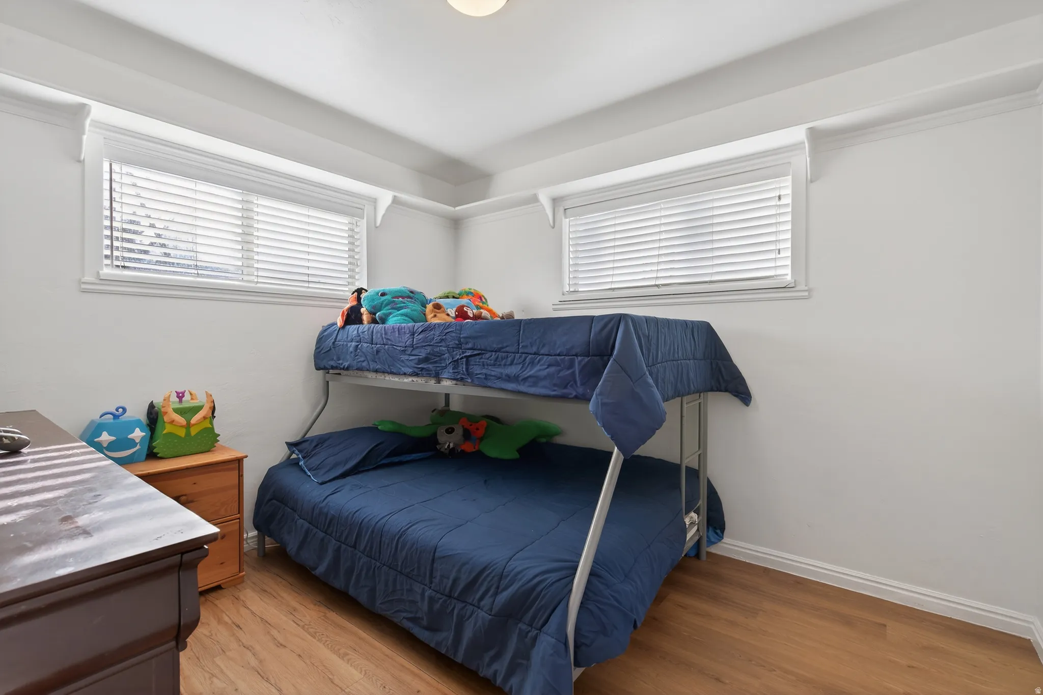Room featuring wood-finish flooring, two windows with white blinds, and white baseboards