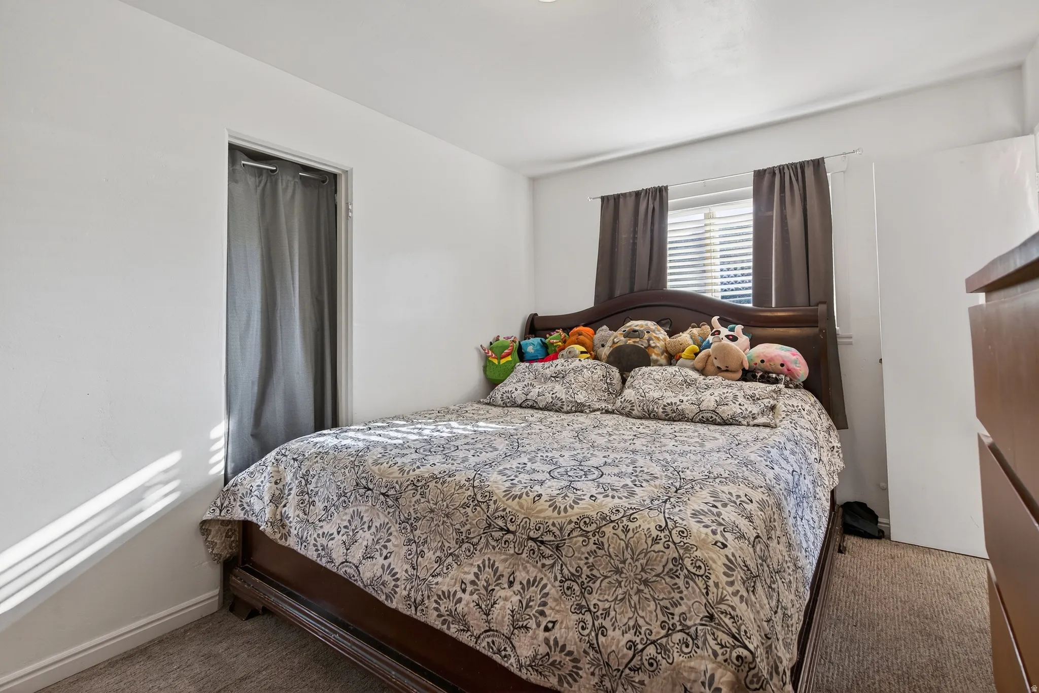 Carpeted room with a window featuring horizontal blinds and dark curtains, complemented by a white door and a closet opening with a fabric curtain