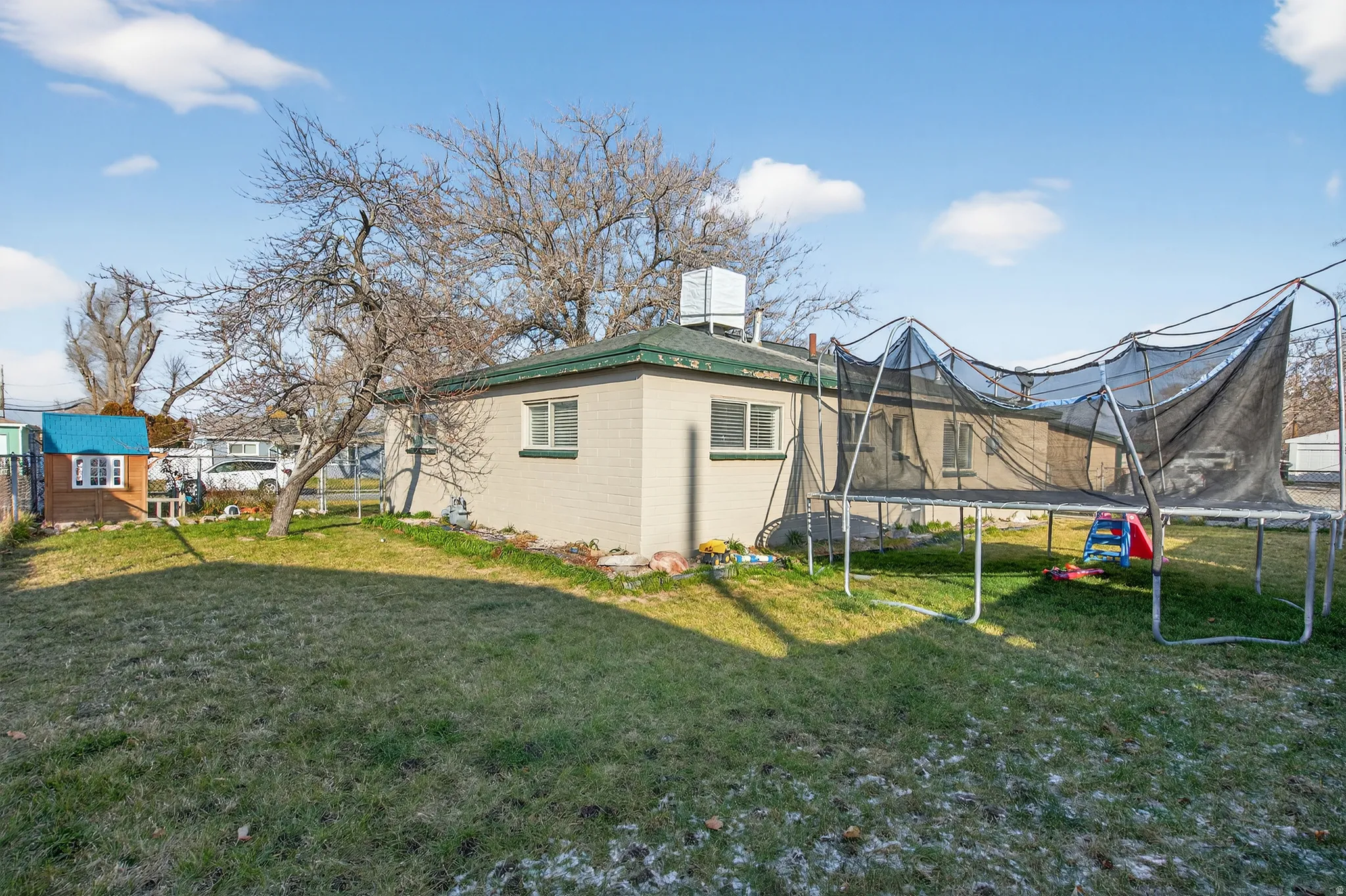 Expansive backyard featuring a partial fence, mature trees, and a green roofline