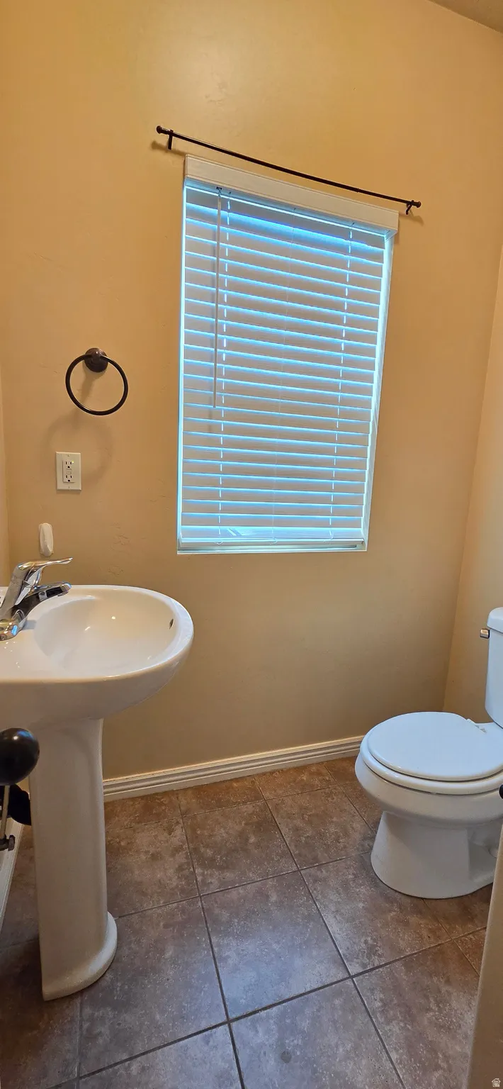 Pedestal sink with chrome faucet, toilet, and window with horizontal blinds