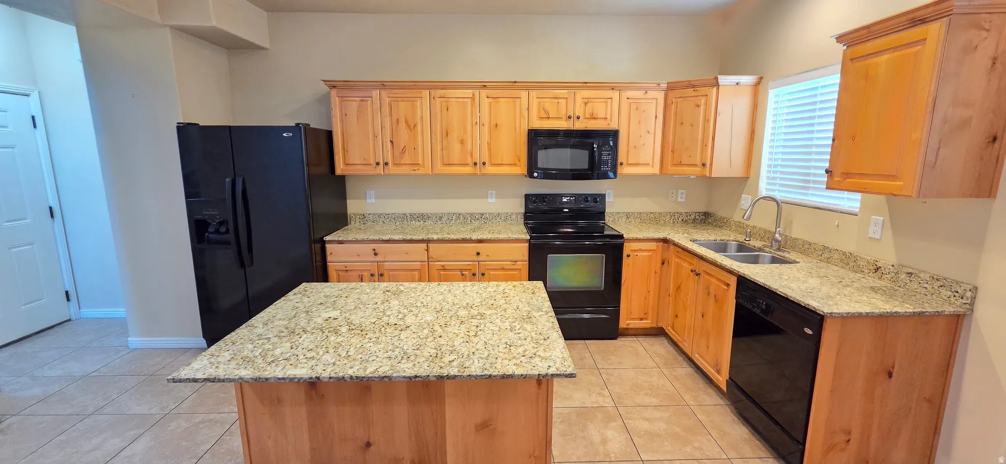 Kitchen featuring light wood cabinetry, stone countertops, black appliances, a double basin sink, and tile flooring