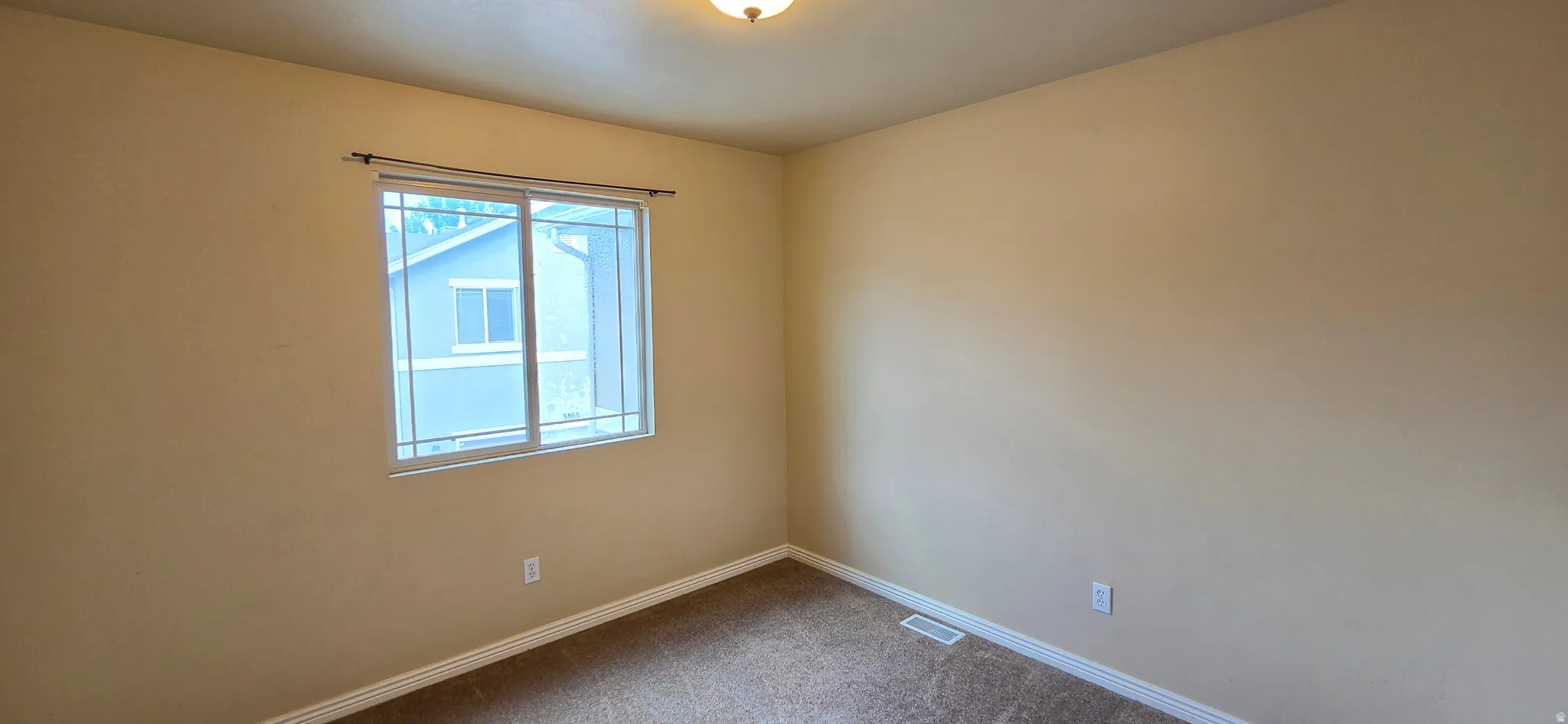 Spacious room featuring neutral-toned walls, a large window with white framing, and dark brown carpeting