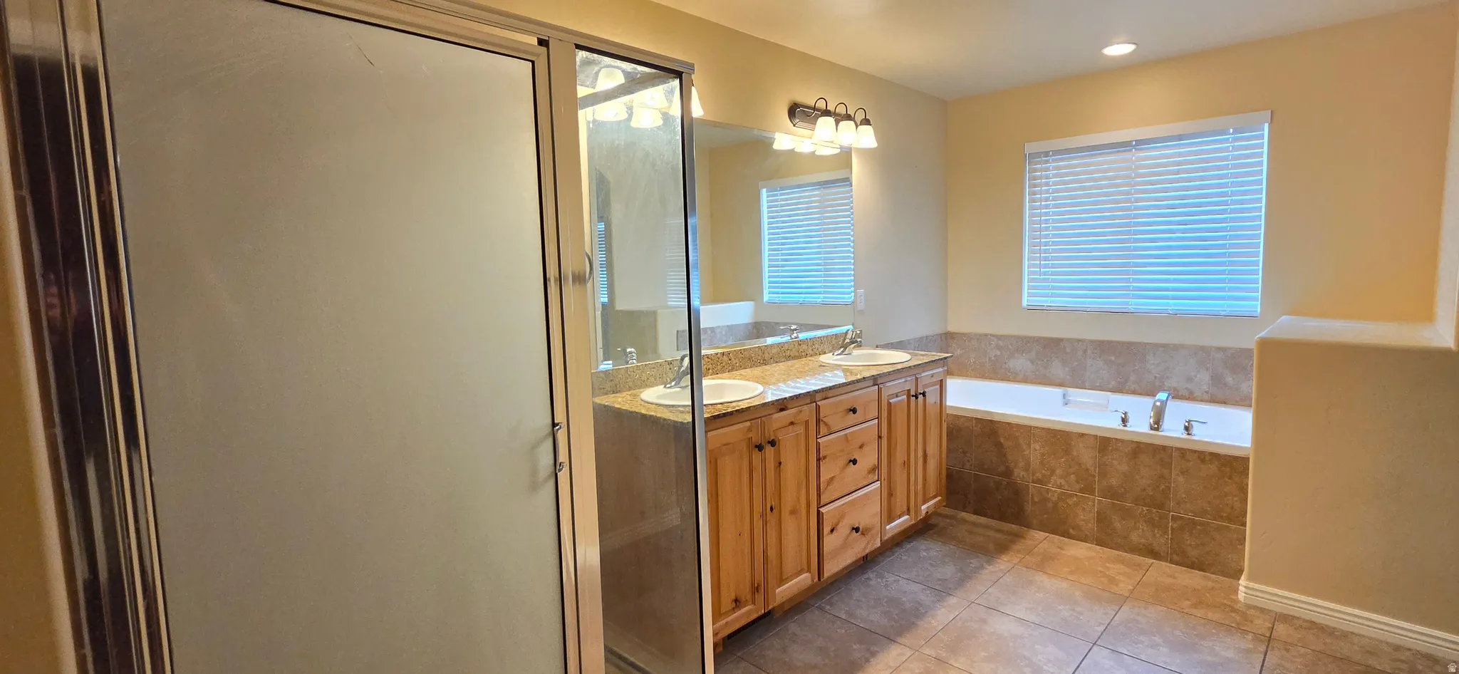 Bathroom featuring a glass-enclosed shower, dual vanity with granite-style countertop, and a built-in bathtub with tiled surround
