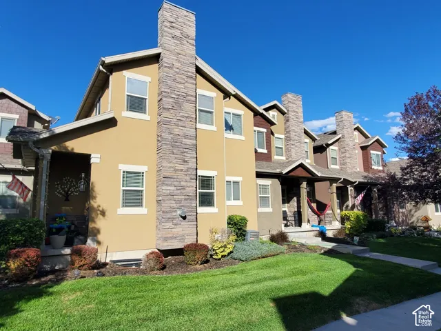 Exterior featuring stucco and stone veneer, multiple windows with blinds, a covered porch, and a manicured lawn