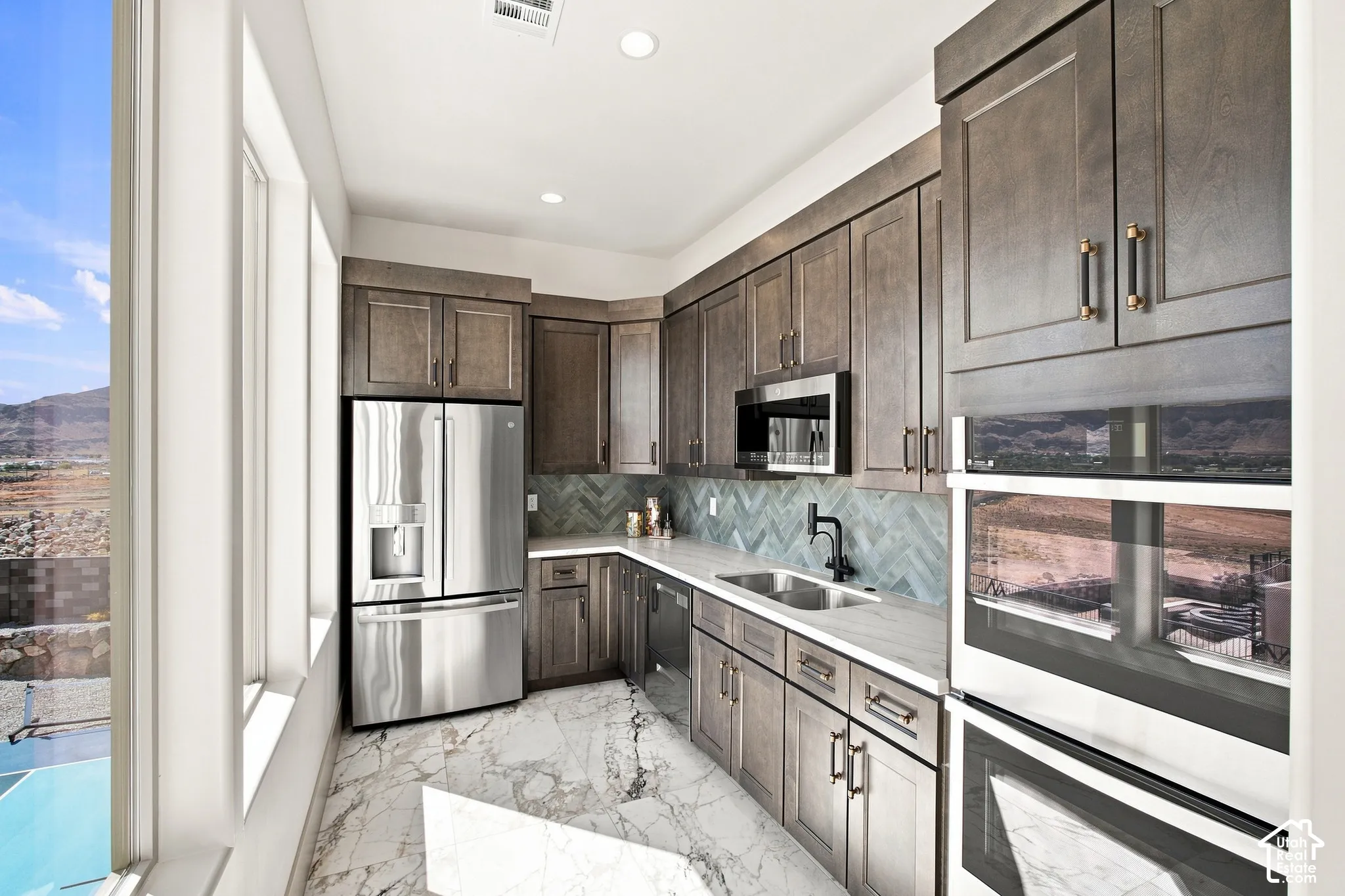 Gourmet kitchen with stainless steel appliances, custom cabinetry, herringbone tile backsplash, double basin sink, and ample natural light
