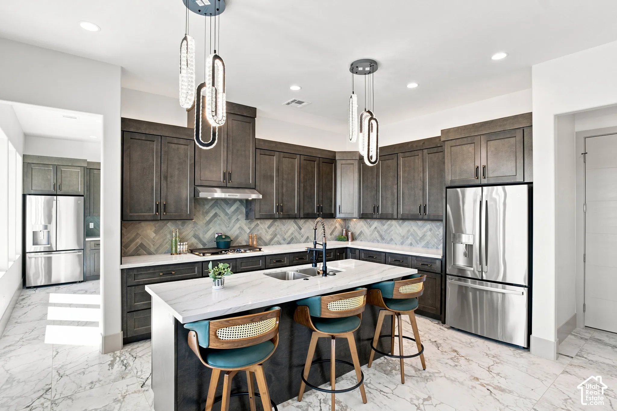 Spacious kitchen featuring an expansive island, dark wood-finish cabinetry, stainless steel appliances, and a herringbone-patterned backsplash