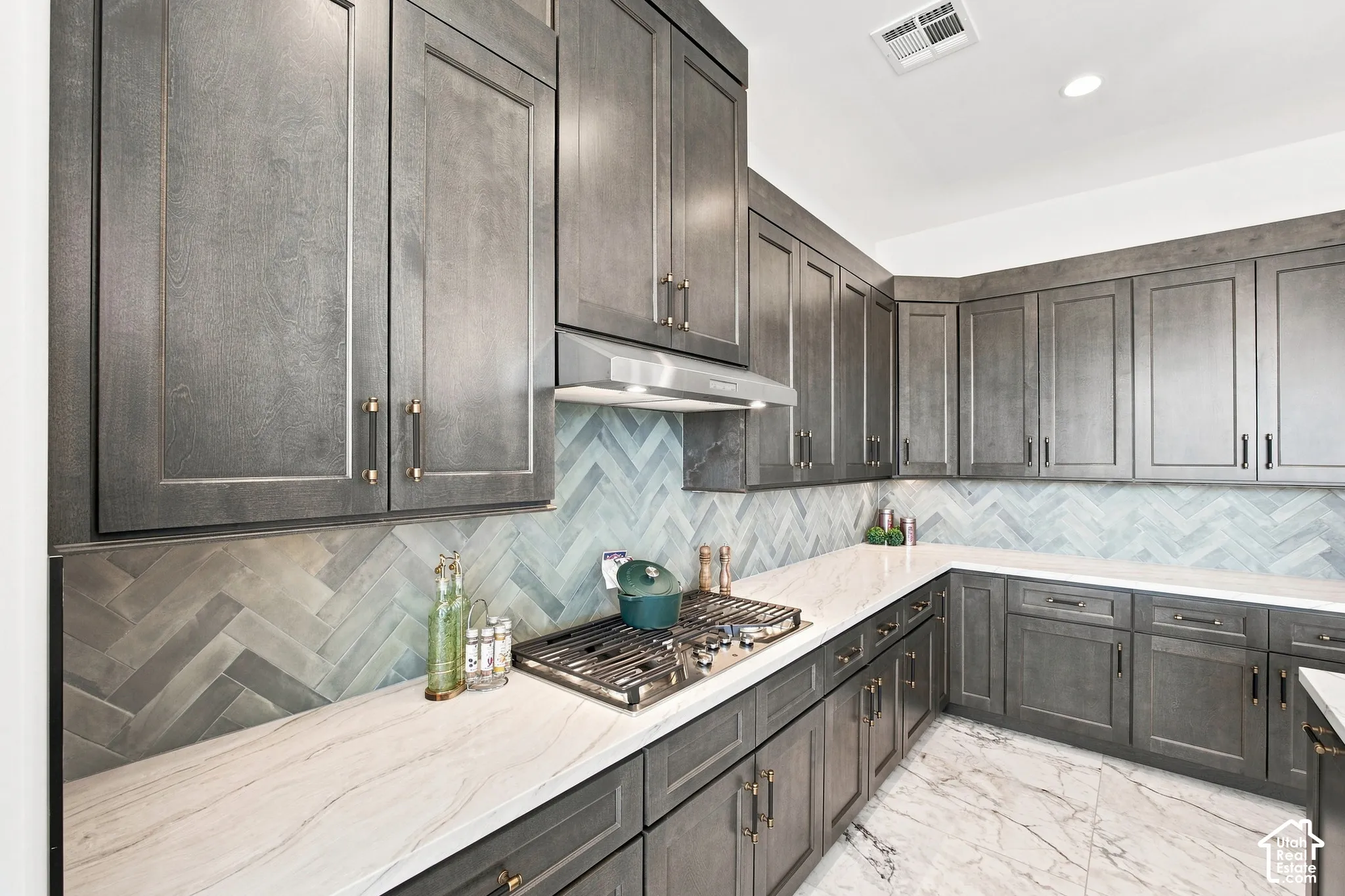Extensive cabinetry with modern hardware, white countertops, herringbone tile backsplash, and a built-in gas range