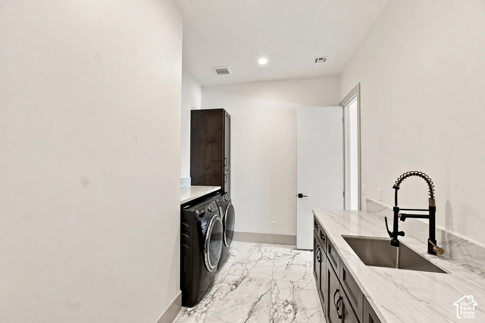 Laundry room featuring marble-look tile flooring, white countertops, built-in cabinetry, an under-mount sink, and a black pull-down faucet