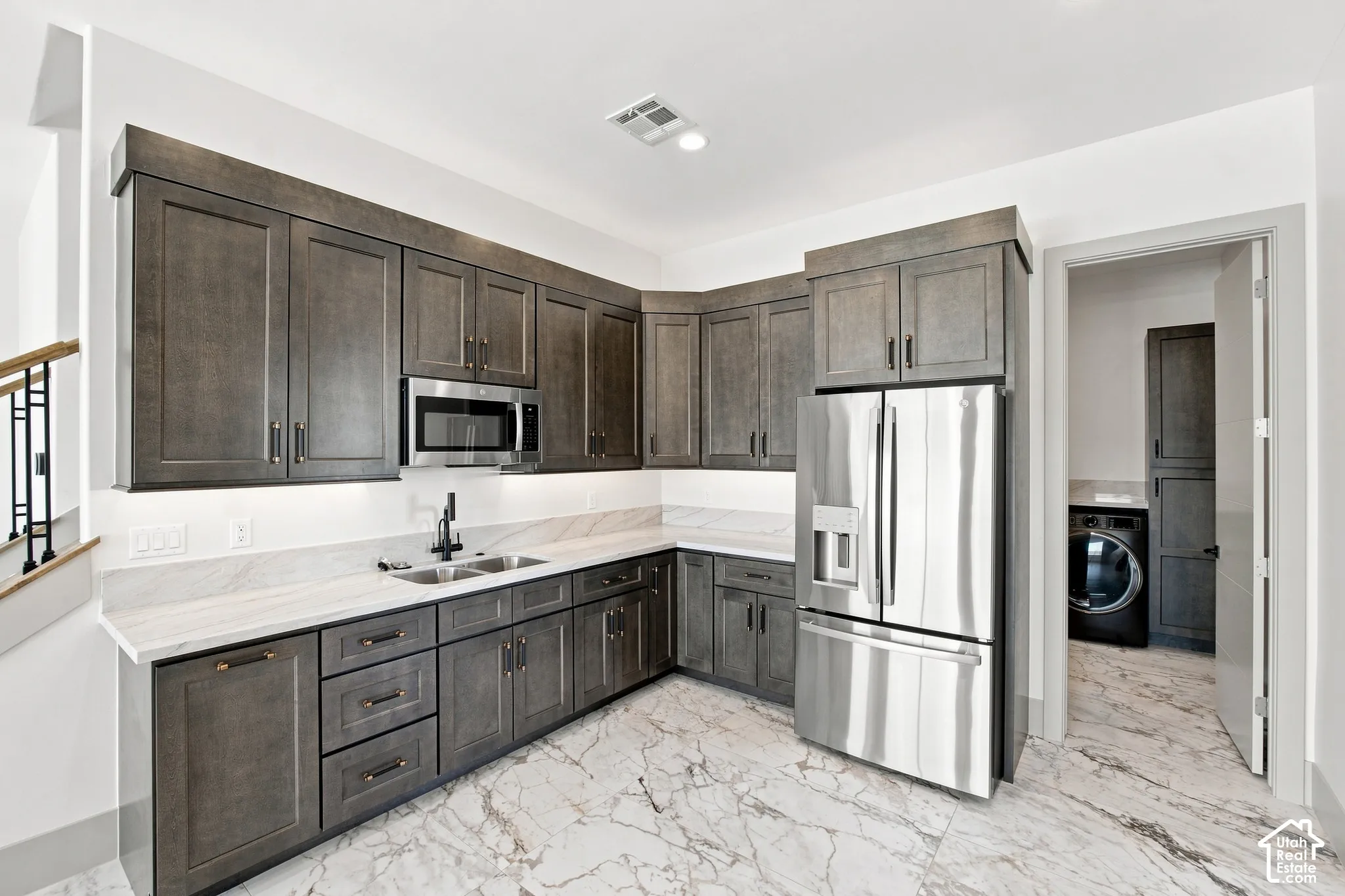Full-height cabinetry, stainless steel appliances, dual basin sink with matte black fixture, white stone countertops, and marble-finish flooring