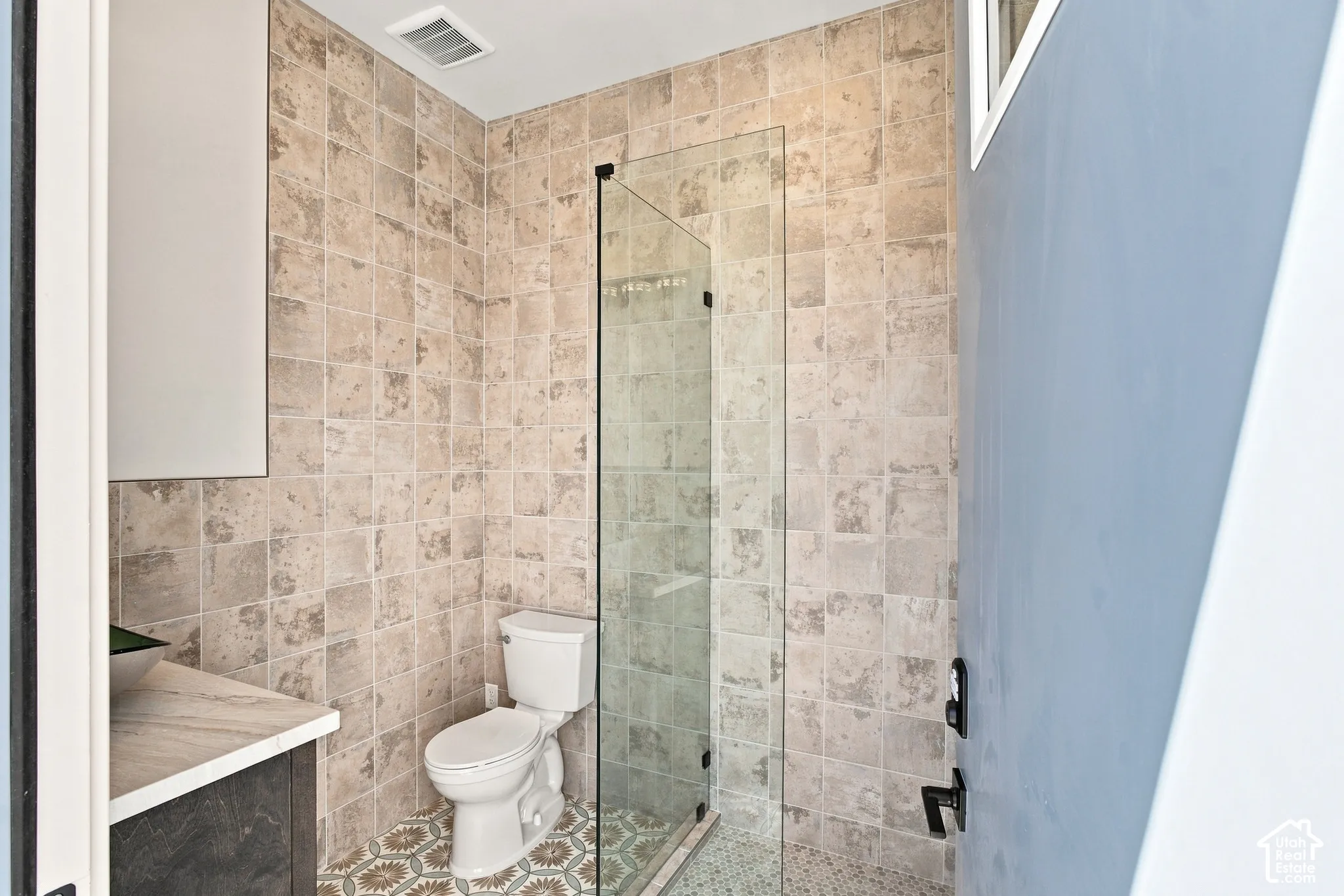 Glass-enclosed shower, floor-to-ceiling tile, patterned floor tile, vanity with countertop, wall-mounted cabinet