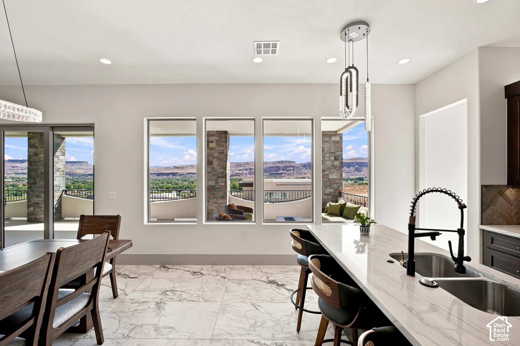 Open-concept living area featuring large format marble-look tile flooring, a kitchen island with dual sinks, and multiple windows overlooking a distant mountain range
