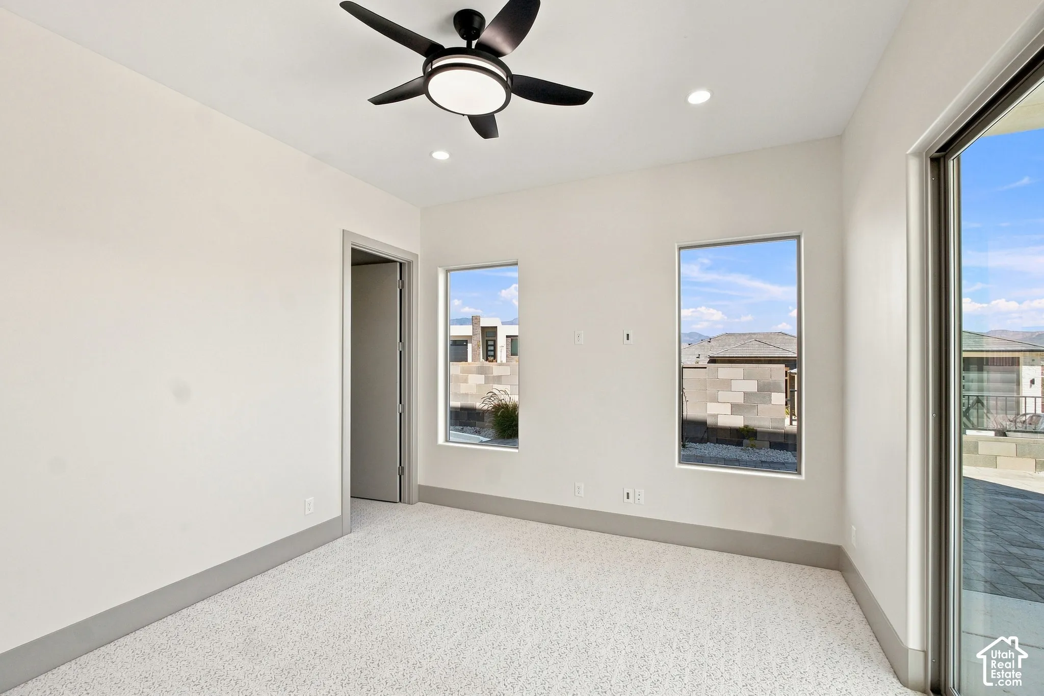 Recessed lighting, ceiling fan fixture, two windows, glass sliding door, and light-toned patterned carpet