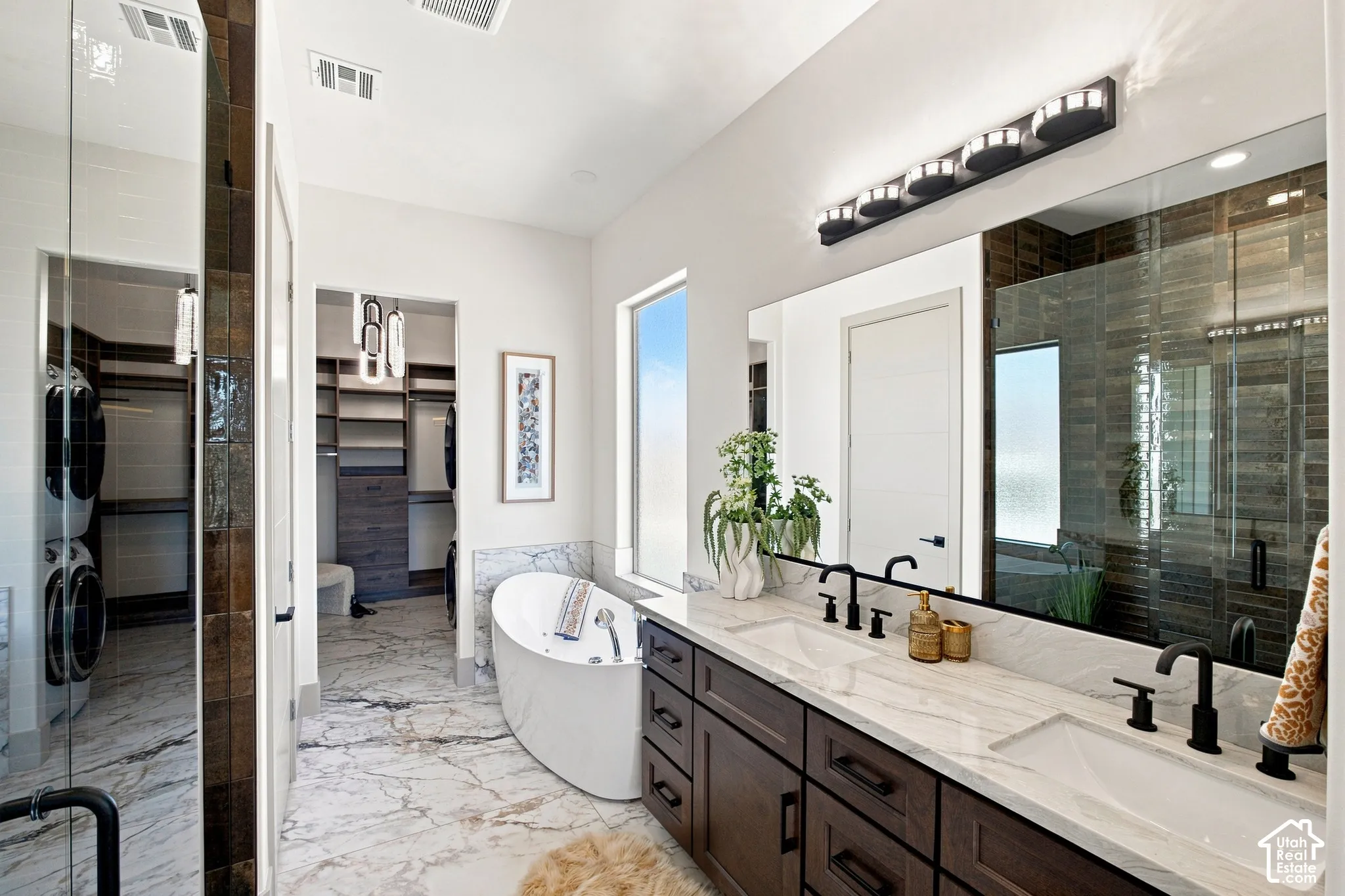 Dual vanity with integrated sinks and matte black fixtures, free-standing soaking tub, walk-in shower with glass enclosure, wood-finish flooring, and a dedicated laundry area