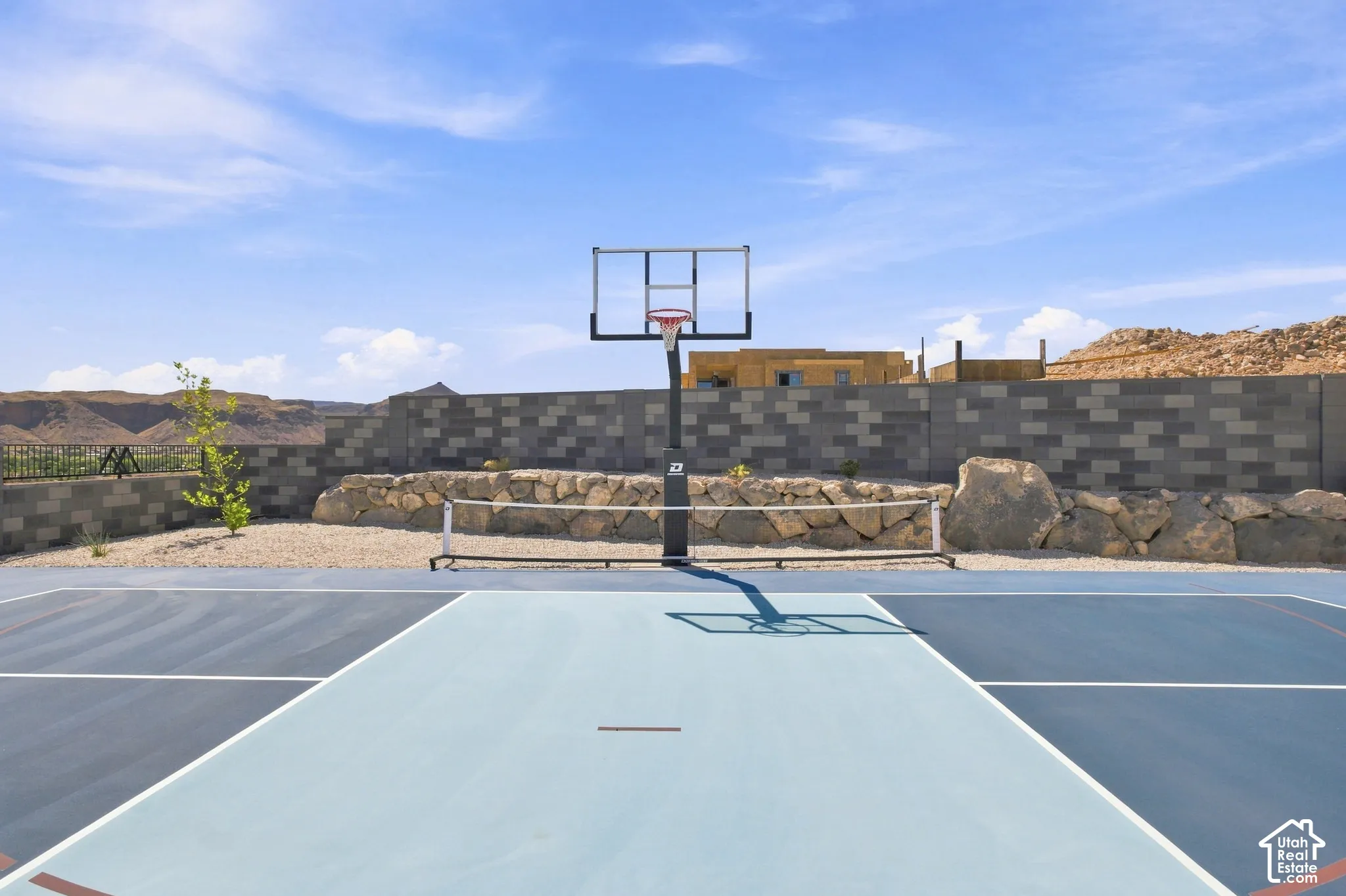 Multi-sport court with basketball hoop and integrated net, set against a block wall and natural rock landscaping