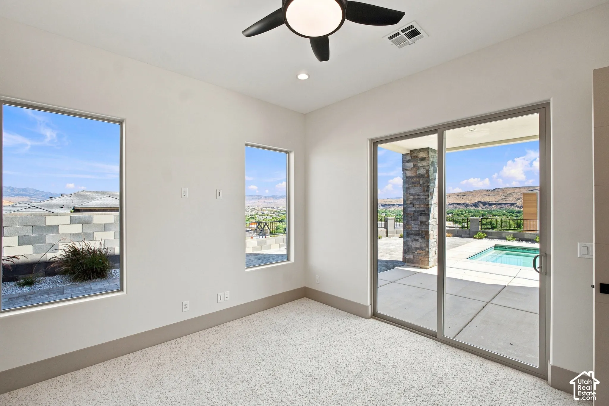Plush carpet flooring, ceiling fan with integrated lighting, multiple windows, and a sliding glass door providing access to an outdoor area with a pool