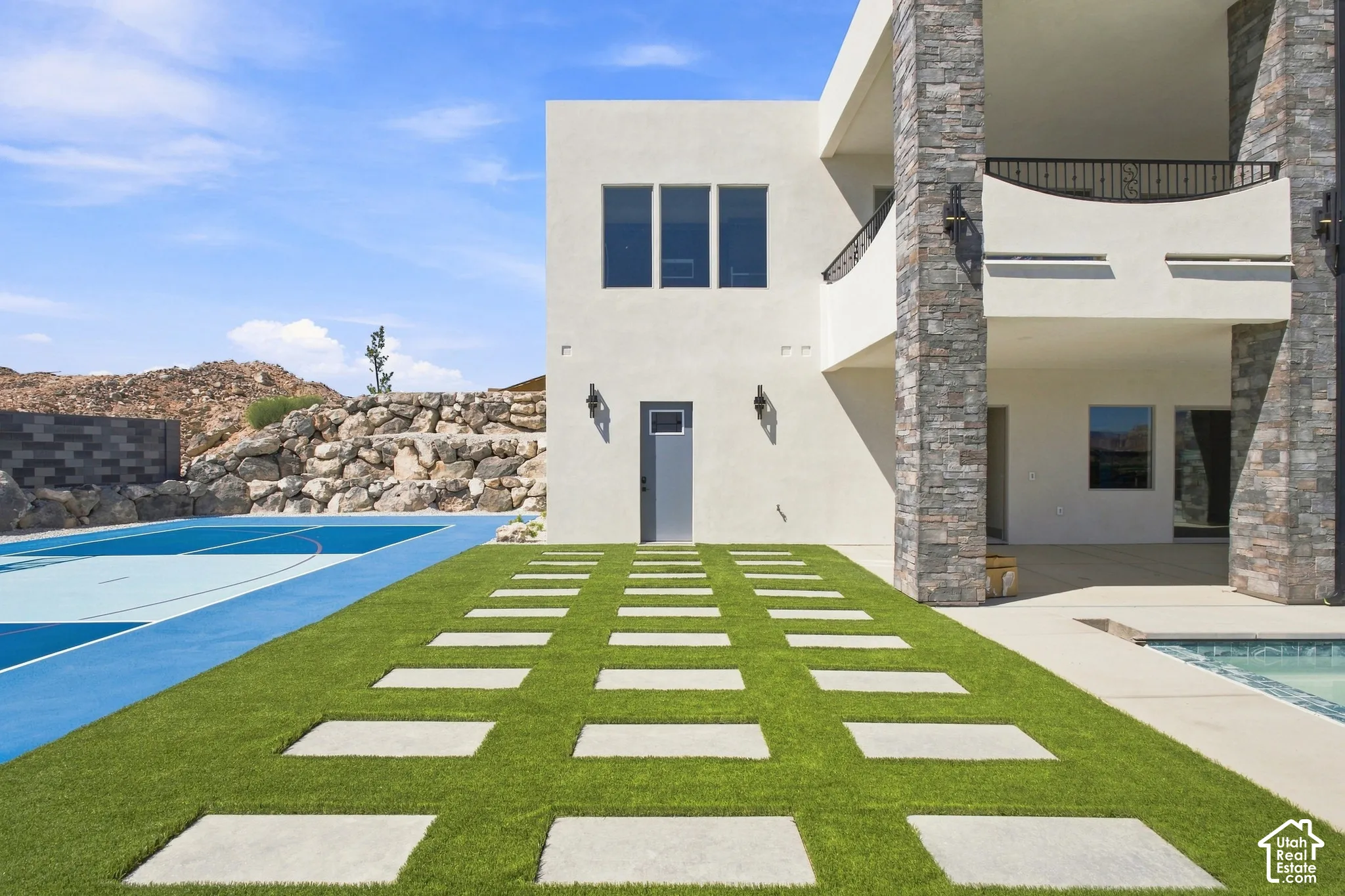 Modern exterior with stone accents, a full-size sports court, an artificial turf pathway with concrete pavers, and an integrated swimming pool