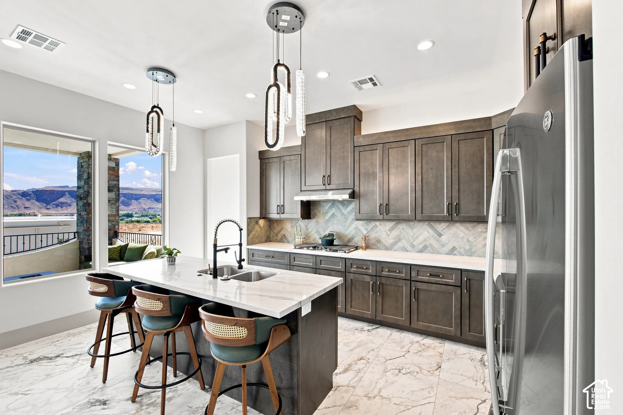 Contemporary kitchen featuring a large island with an undermount sink, a herringbone tile backsplash, gray cabinetry, and stainless steel appliances