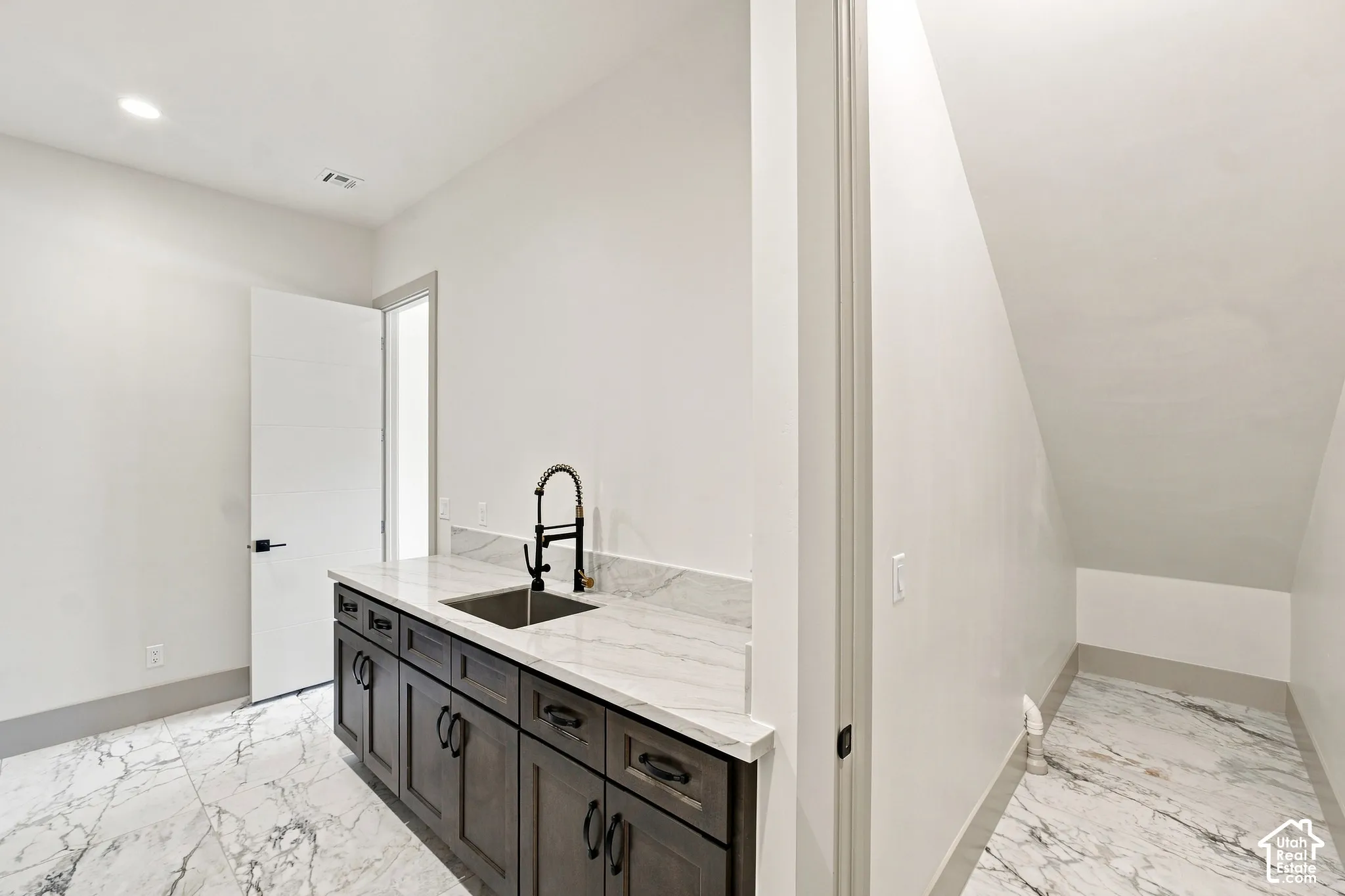 White marble-look flooring, dark wood-finish cabinetry, and a stainless steel sink with a black faucet