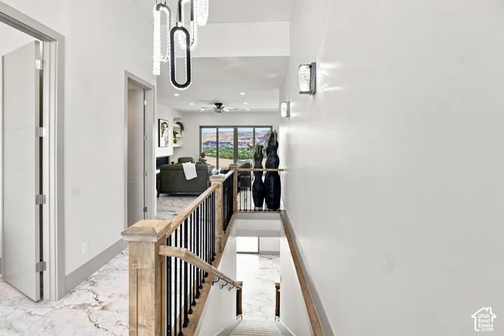 Hallway featuring modern crystal chandelier, sconce lighting, wood-finish stair railing with black spindles, and marble-finish flooring