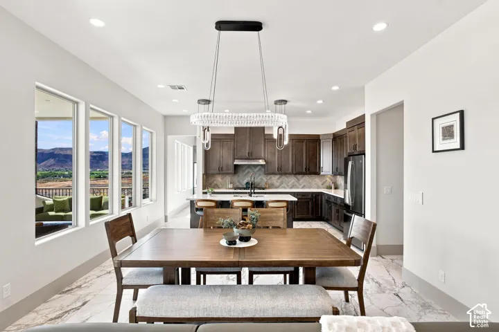 Open-concept living area with a contemporary chandelier, large picture windows, and a kitchen featuring dark wood cabinetry, a herringbone tile backsplash, and a central island