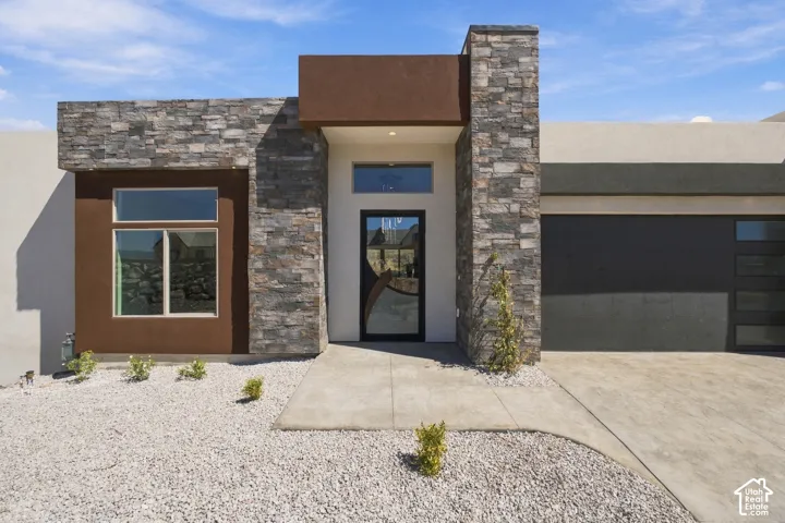Contemporary exterior showcasing stacked stone accents, a dark-framed glass entry door, and an integrated garage with frosted glass panels