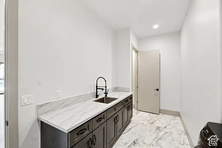 Integrated utility sink with a matte black gooseneck faucet, white-veined countertop, dark wood-finish cabinetry, and large format floor tiling