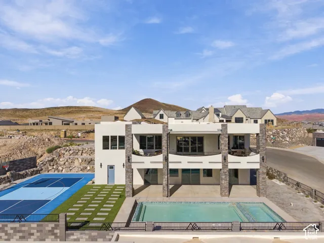Contemporary exterior with multiple balconies, stacked stone accents, a rectangular swimming pool, a blue sports court, and artificial turf with paver pathways