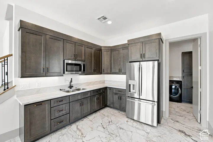 Full-height cabinetry, stainless steel appliances, dual basin sink with matte black fixture, white stone countertops, and marble-finish flooring