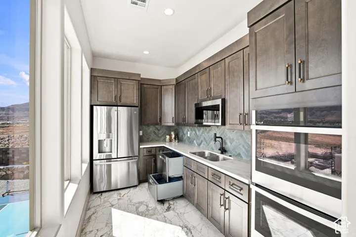 Full-height windows, rich wood-finish cabinetry, stainless steel appliances, herringbone tile backsplash, and marble-finish flooring