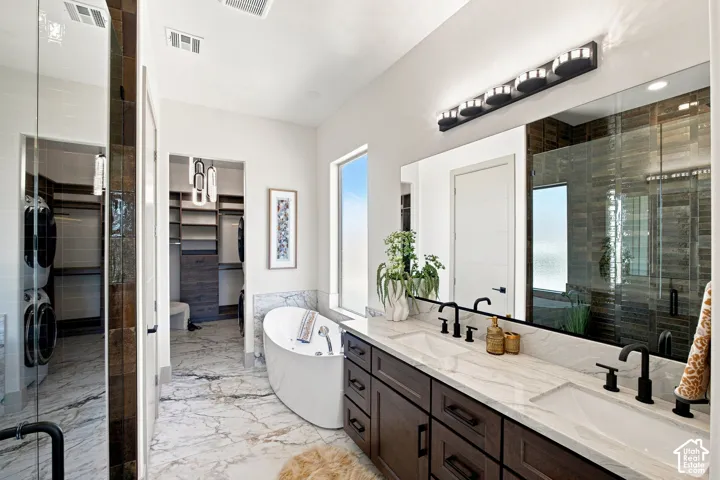 Dual vanity with integrated sinks and matte black fixtures, free-standing soaking tub, walk-in shower with glass enclosure, wood-finish flooring, and a dedicated laundry area