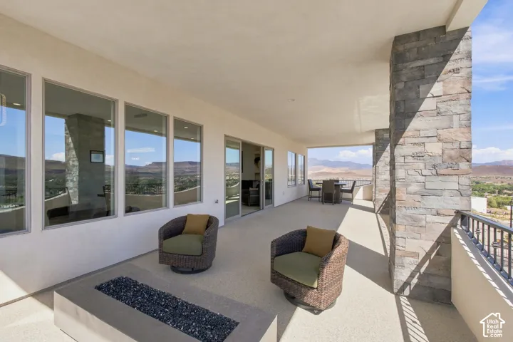 Expansive covered patio featuring a concrete fire pit, stone-clad columns, multiple large windows, and a black wrought iron railing