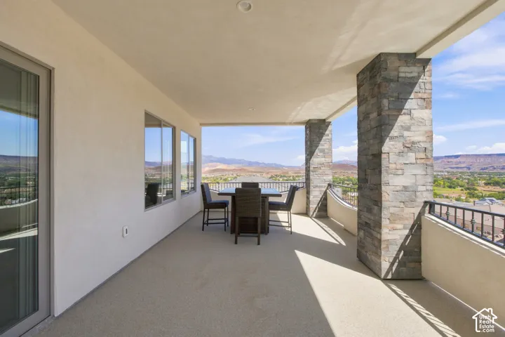 Expansive covered balcony featuring stone-clad pillars, a light-colored stucco exterior, and a durable flooring surface