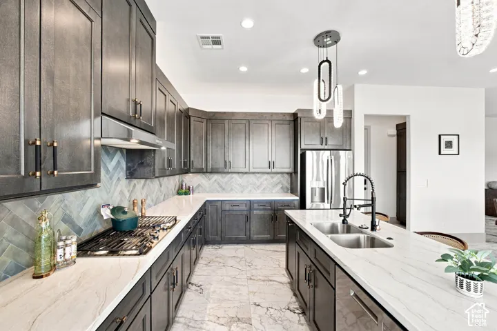 Kitchen featuring dark wood-finish cabinetry, light-toned countertops, stainless steel appliances, a herringbone tile backsplash, and recessed lighting