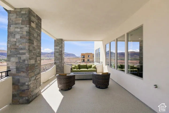 Covered outdoor patio featuring stone-clad pillars, stucco exterior, and a metal railing