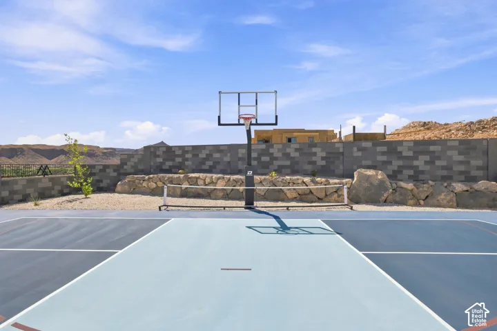 Multi-sport court with basketball hoop and integrated net, set against a block wall and natural rock landscaping