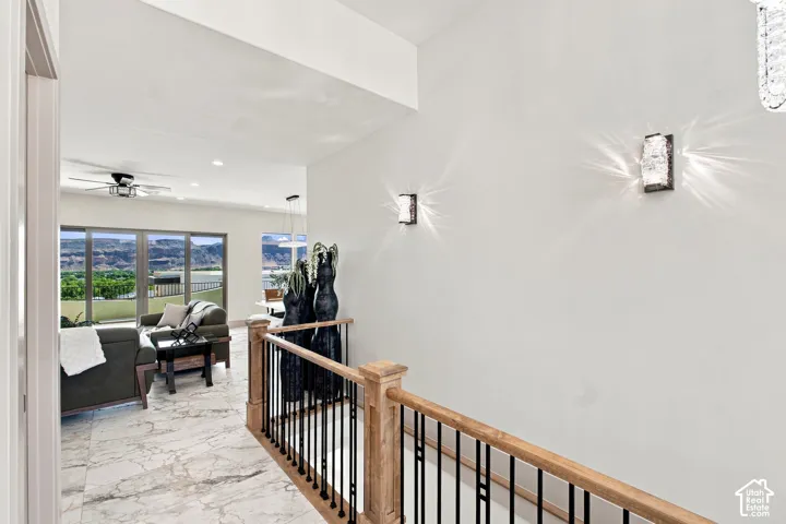 Hardwood railing with black metal spindles, stone-finish tile flooring, recessed lighting, and wall-mounted sconces