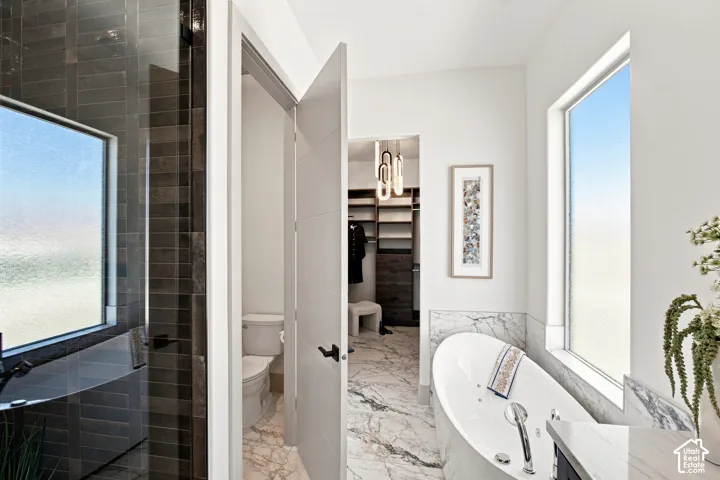Freestanding soaking tub with polished chrome fixtures, white marble tile flooring, and a glass-enclosed shower with dark rectangular wall tile