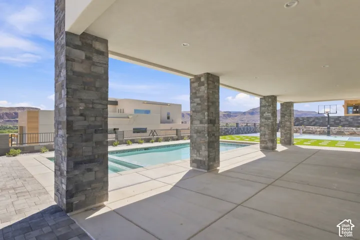 Covered patio with stacked stone pillars, an integrated swimming pool, and an artificial turf sport court
