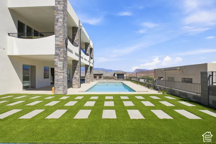 Exterior featuring multiple balconies, stone-clad architectural pillars, a rectangular swimming pool, and a patterned lawn with square pavers
